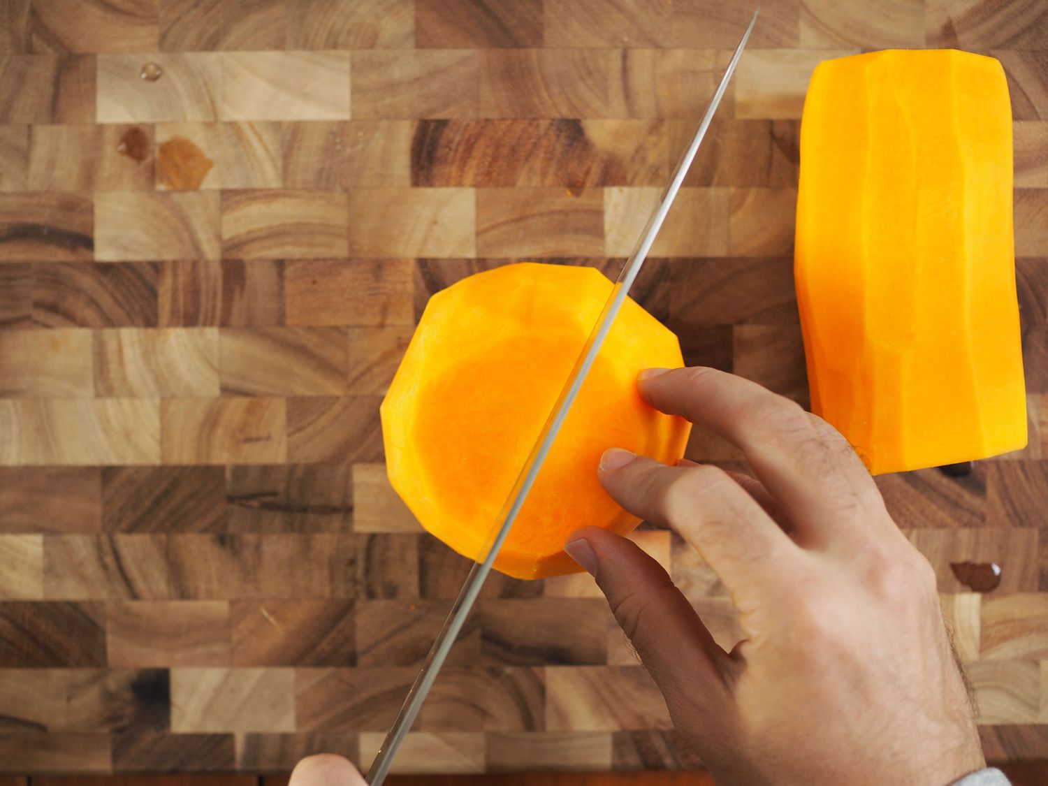 A knife about to cut the body of a butternut squash in half so that the seeds can be removed.