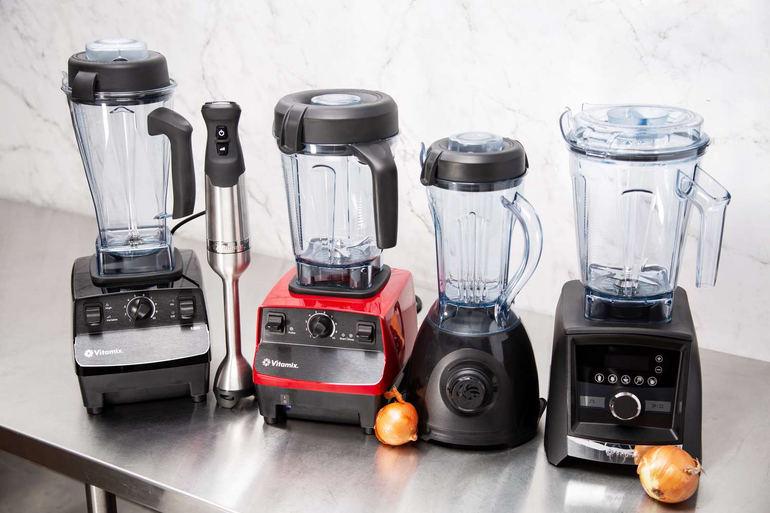Four Vitamix blenders and an immersion blender on a kitchen countertop