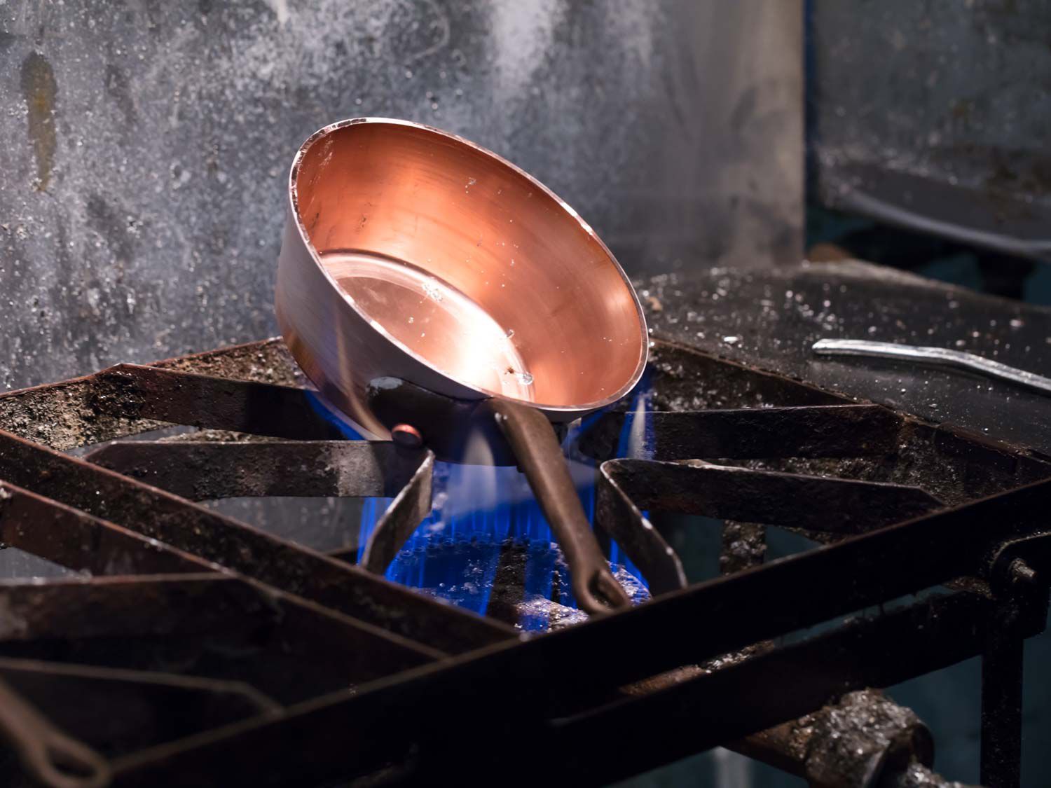 A copper pot heating on an open flame before tin is added to its interior.