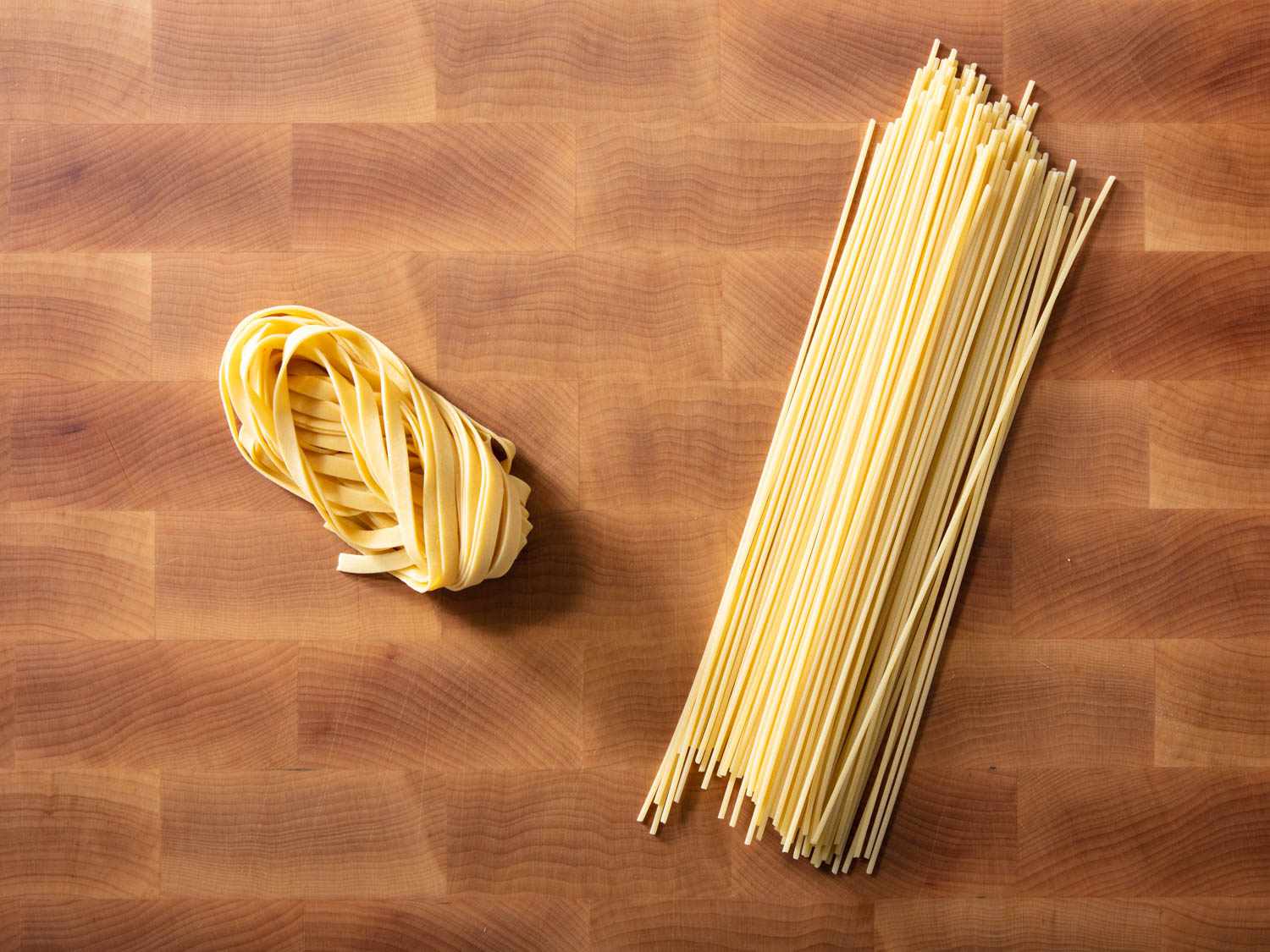 Fresh pasta sits on a cutting board next to some dried spaghetti