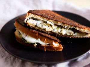 Closeup of a halved and shingled Spinach and Artichoke Grilled Cheese Sandwich, served on a black plate.
