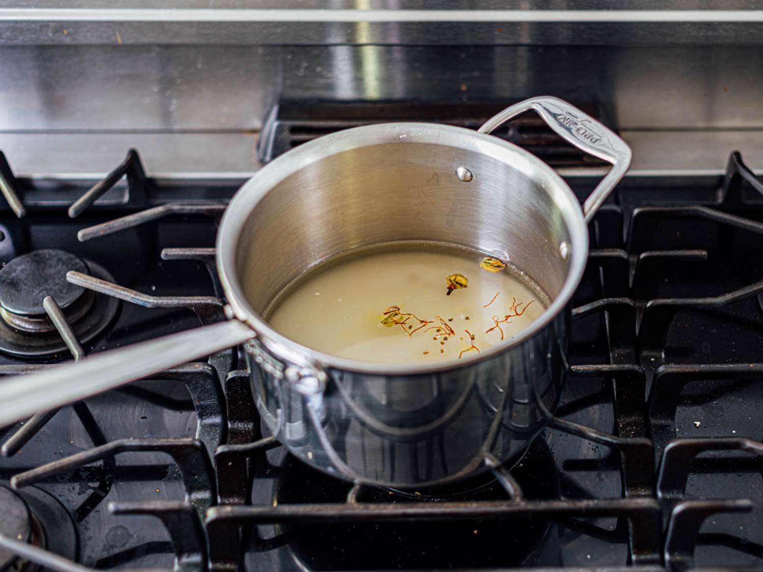 A saucepan on a stovetop filled with ingredients for gulab jamun syrup.