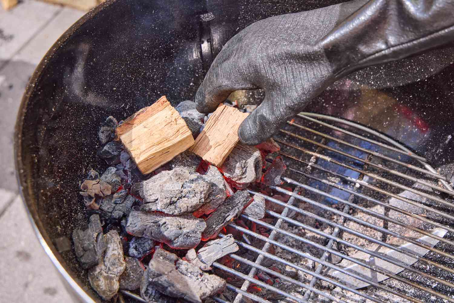 A hand adding wood chips on top of coals in the Weber Original Kettle Premium 22-Inch Charcoal Grill