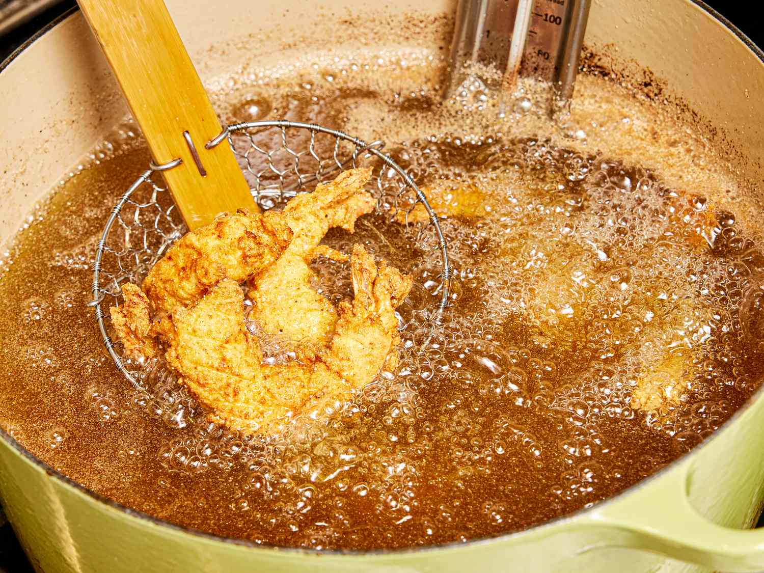 Southern fried shrimp being lifted from hot oil with a spider skimmer in a cooking pot