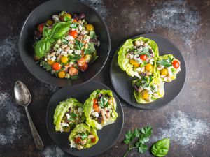 Overhead view of Quick-Marinated White Bean Salad and Feta Lettuce Cups, served on black plates next to a black bowl full of extra bean salad.