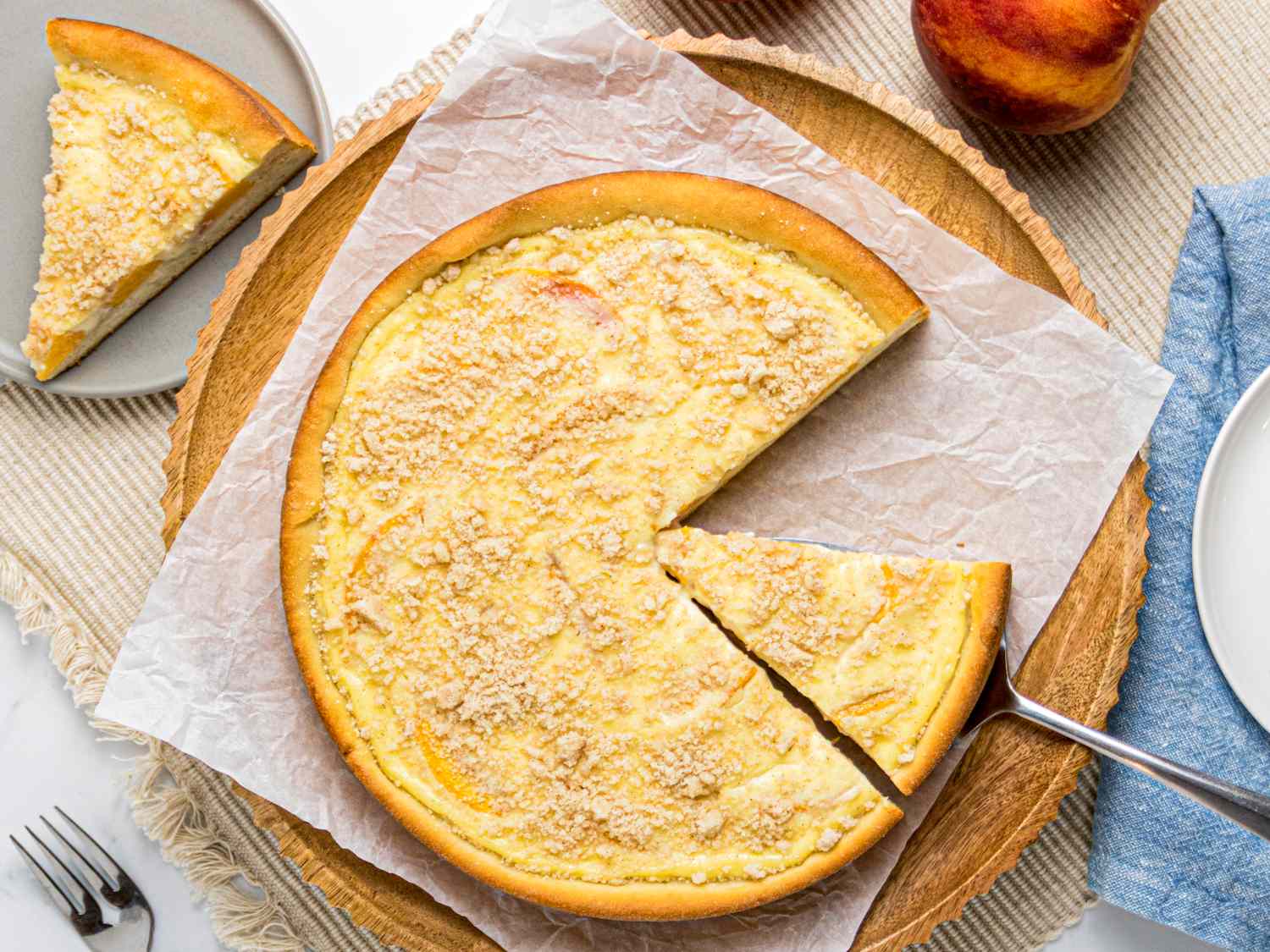 A plate with a sliced kuchen on a table with peach and fork nearby