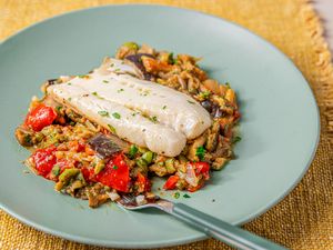 A plate of cod fillet served on a bed of caponata placed on a greencolored plate with a fork