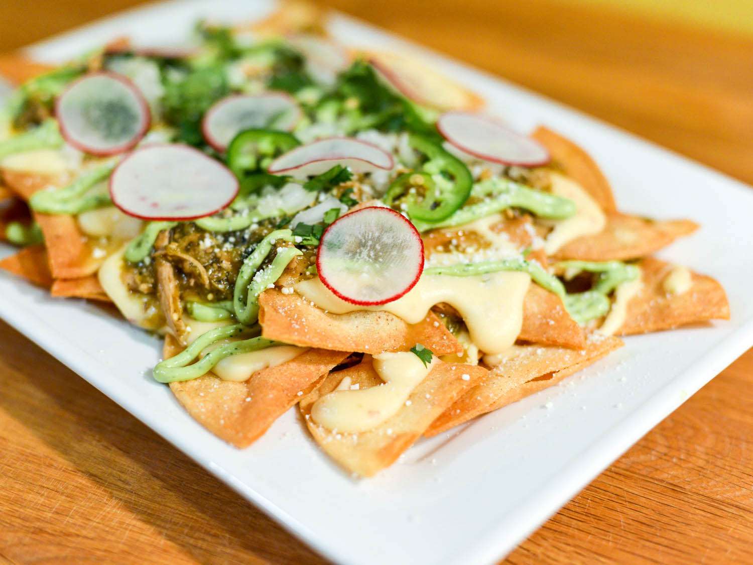 A plate of tortilla chips topped with chile verde, chicken, sliced radish, and jalapeño slices