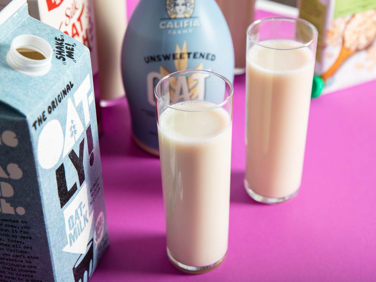 Two tall glasses of oatmilk placed next to their respective cartons.