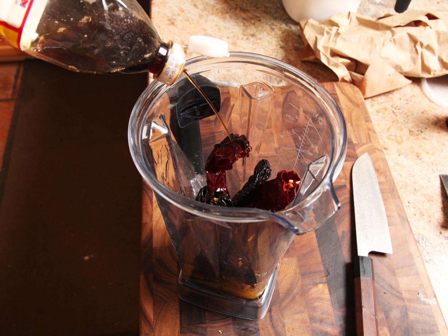 Adding fish sauce to a blender containing dried chiles to make carne asada marinade.