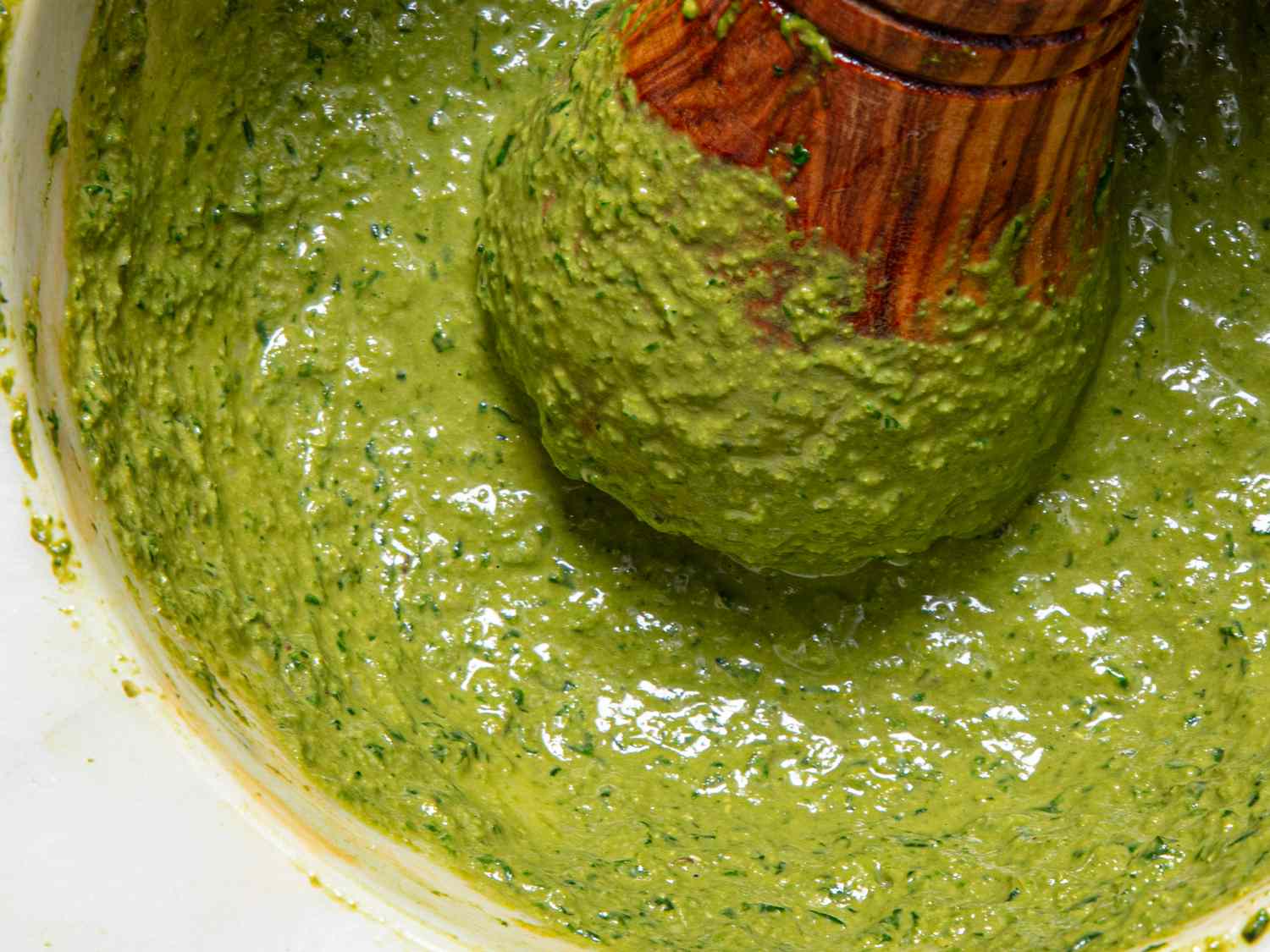 Closeup of a bowl of pesto being mixed with a wooden pestle