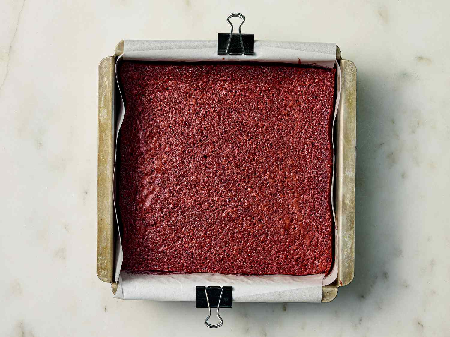 Cooked brownies in a square tin on a white marble surface 