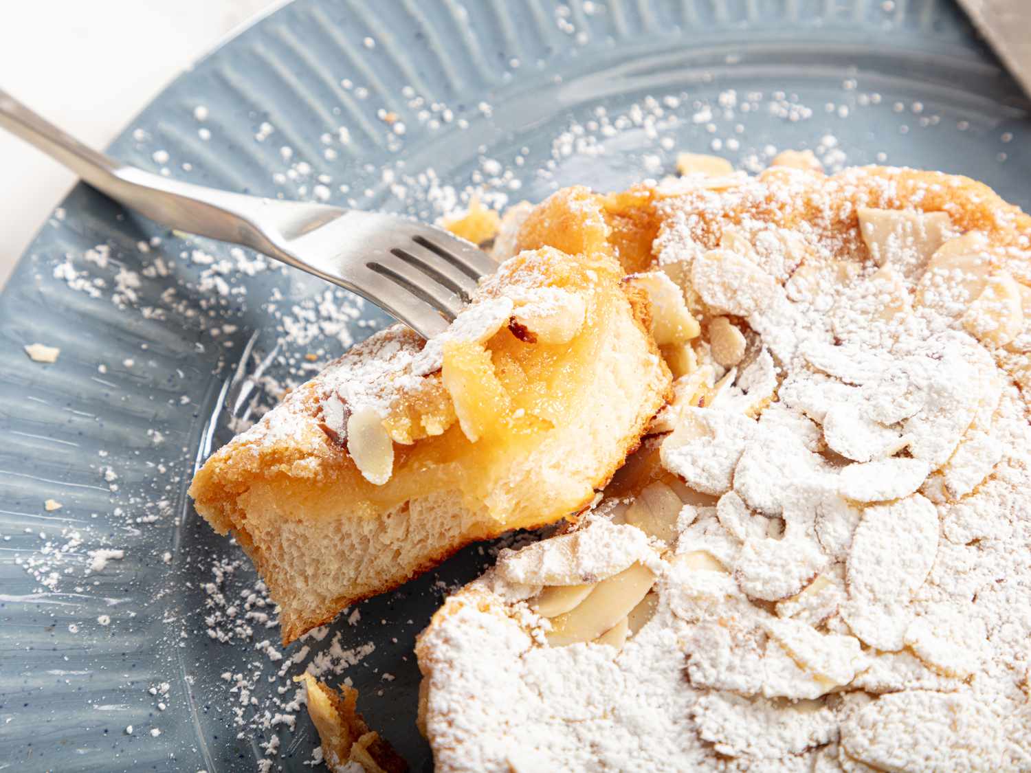 Bostock with a fork holding up a corner bit of it, on a blue plate covered in powdered sugar