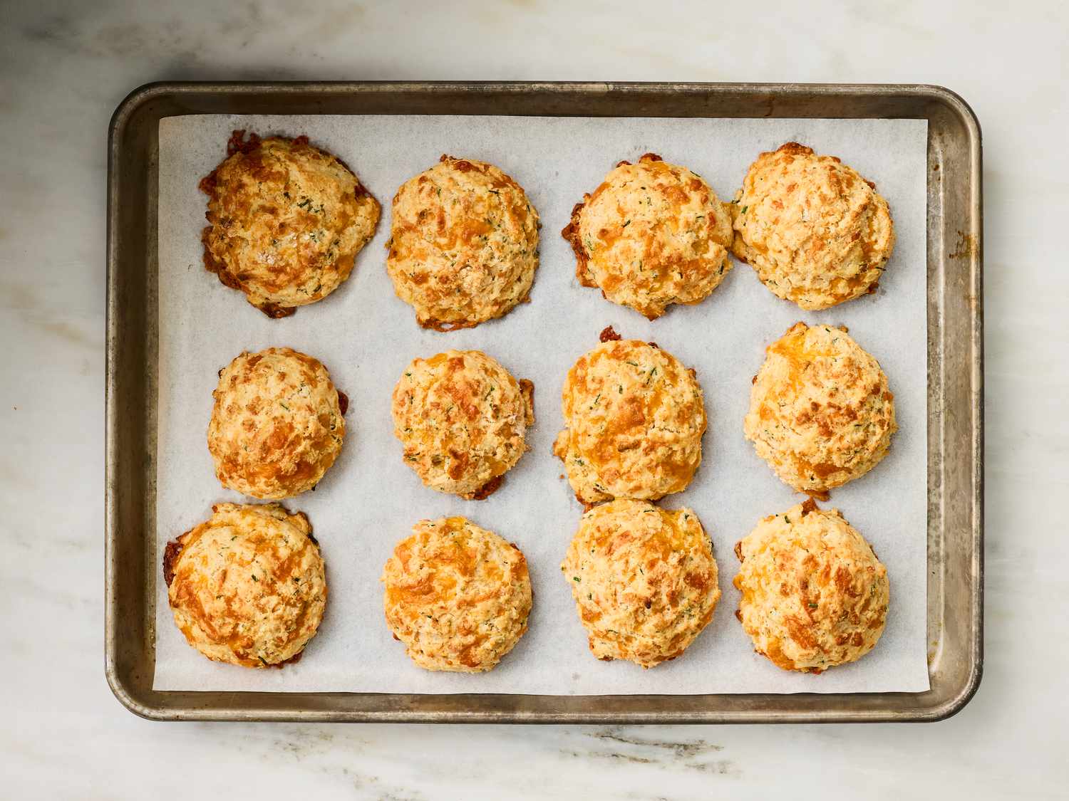 A baking tray with twelve chive cheddar drop biscuits placed on parchment paper