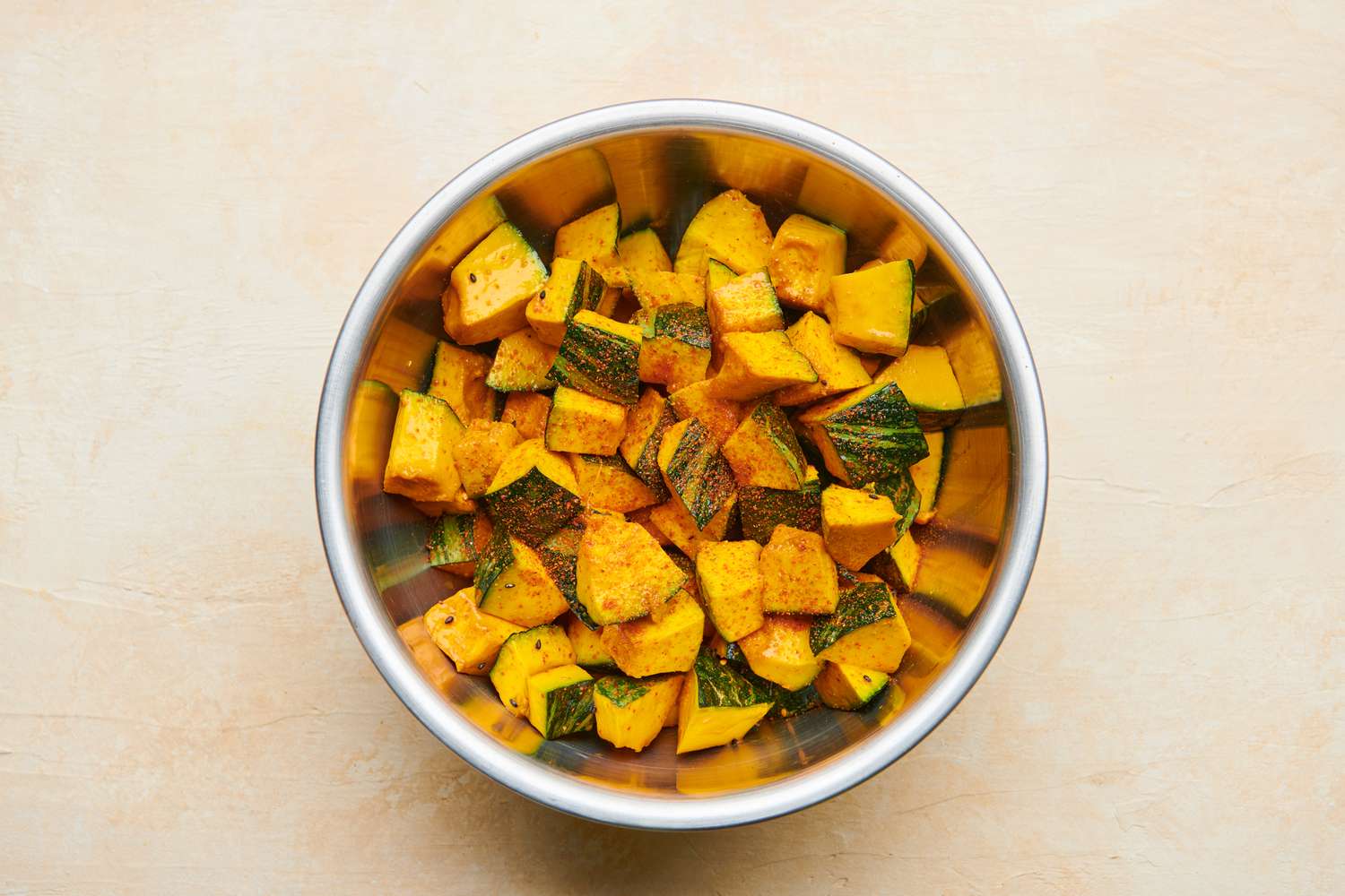 The chopped, uncooked kabocha squash in a metal bowl and tossed with the shichimi togarashi.