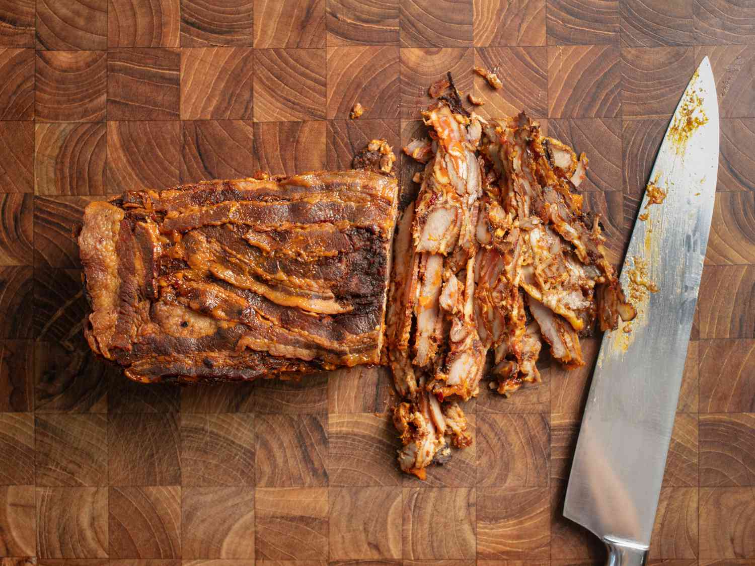 Loaf of cooked al pastor meat sliced up on wooden cutting board 