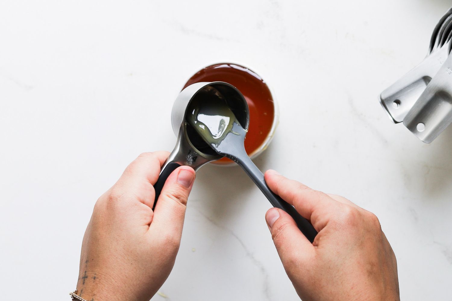 Hands holding and using measuring cups over a bowl with another set of nested cups on the side
