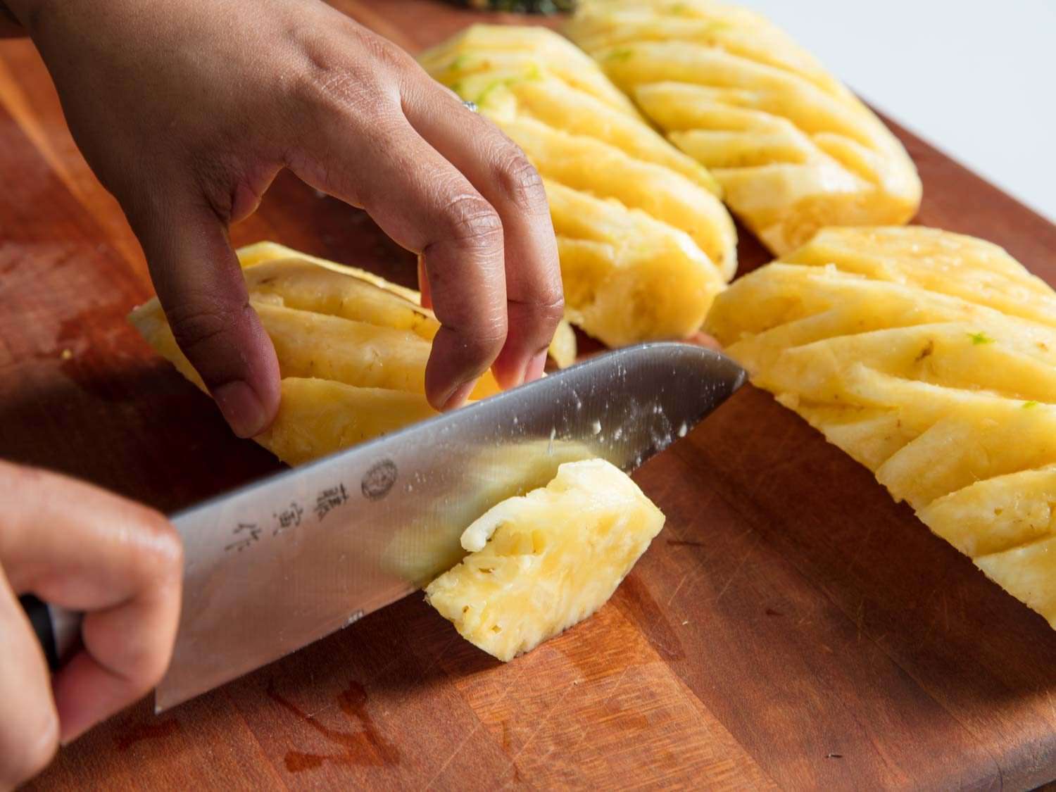 A knife cutting slices of a pineapple.
