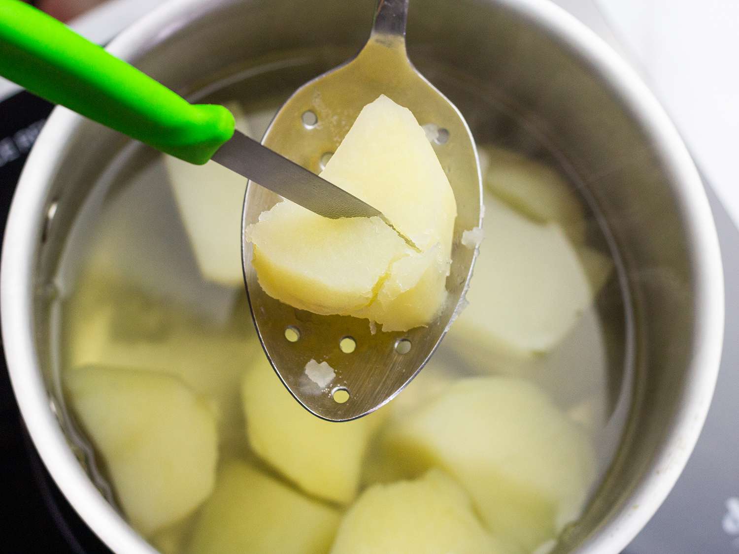 paring knife piercing a piece of boiled potato over a pot of water
