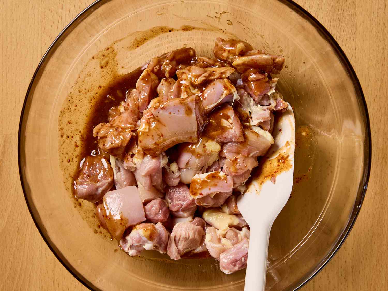 Marinated chicken pieces in a bowl with a white spatula, prepared for skewering