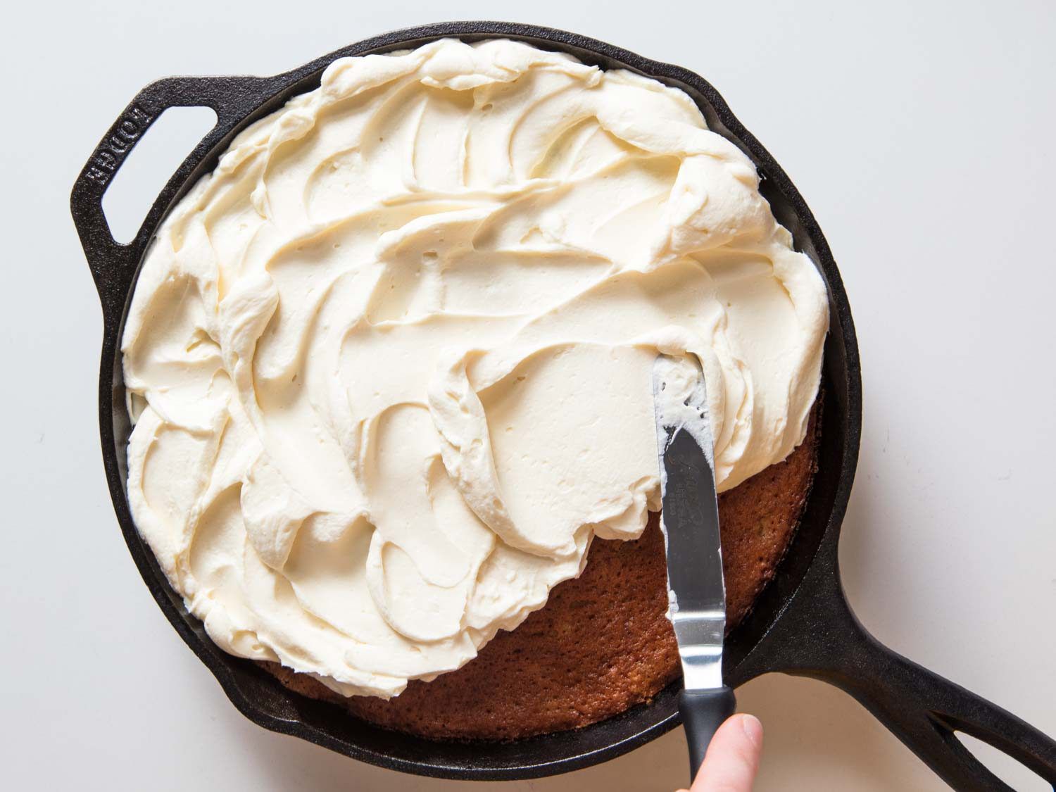 Slathering cream cheese frosting on hummingbird cake.