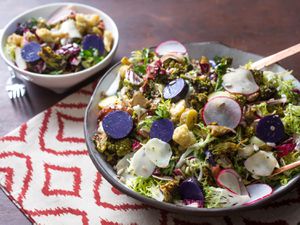 A big bowl of brassica salad with wooden serving utensils
