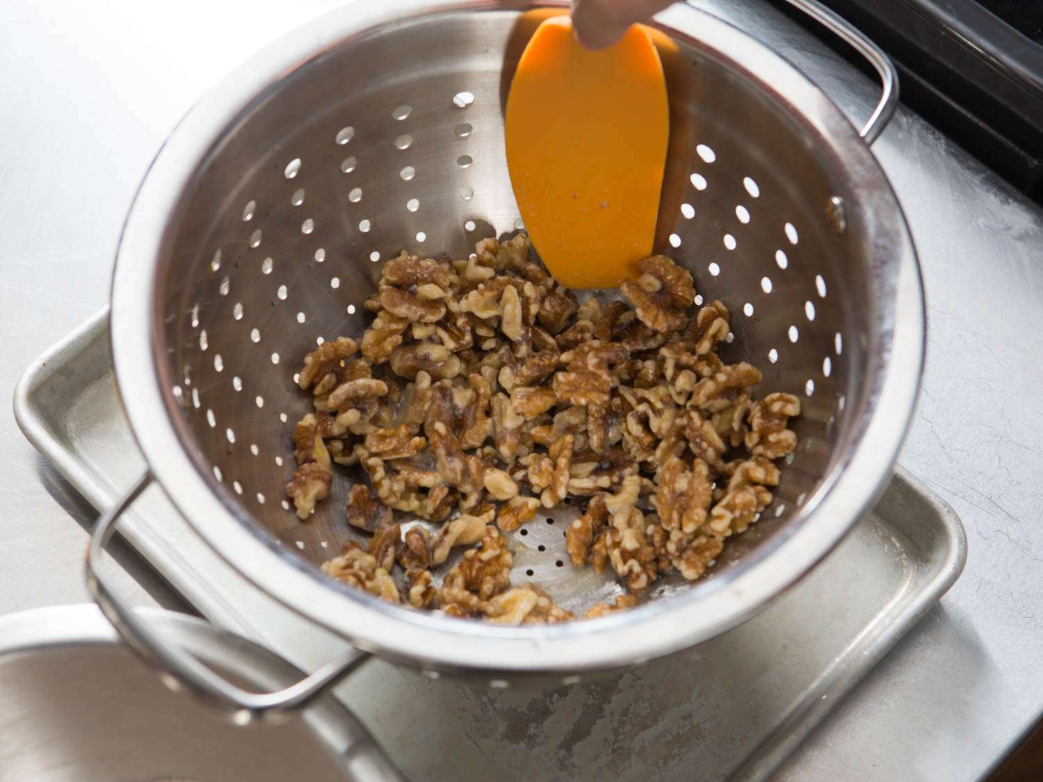 Draining egg white- and orange juice-coated walnuts in a colander.