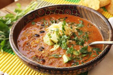 A bowl of creamy enchilada soup, topped with cilantro, avocado, green onion, and shredded cheese.