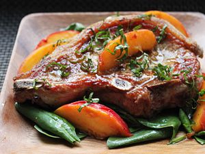 A plated pork chop with fresh peaches and basil.