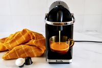 Espresso machine brewing coffee into a glass mug yellow cloth and coffee pods nearby