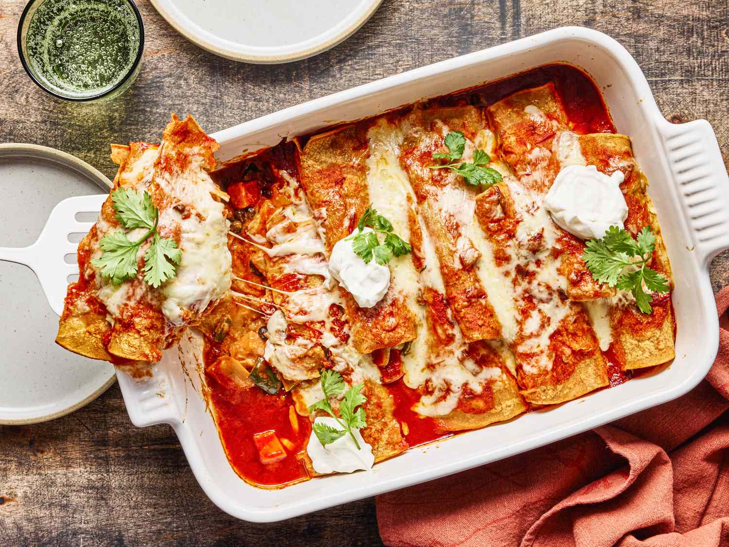 Freshly baked sweet potato enchiladas topped with melted cheese cilantro and dollops of cream served in a casserole dish
