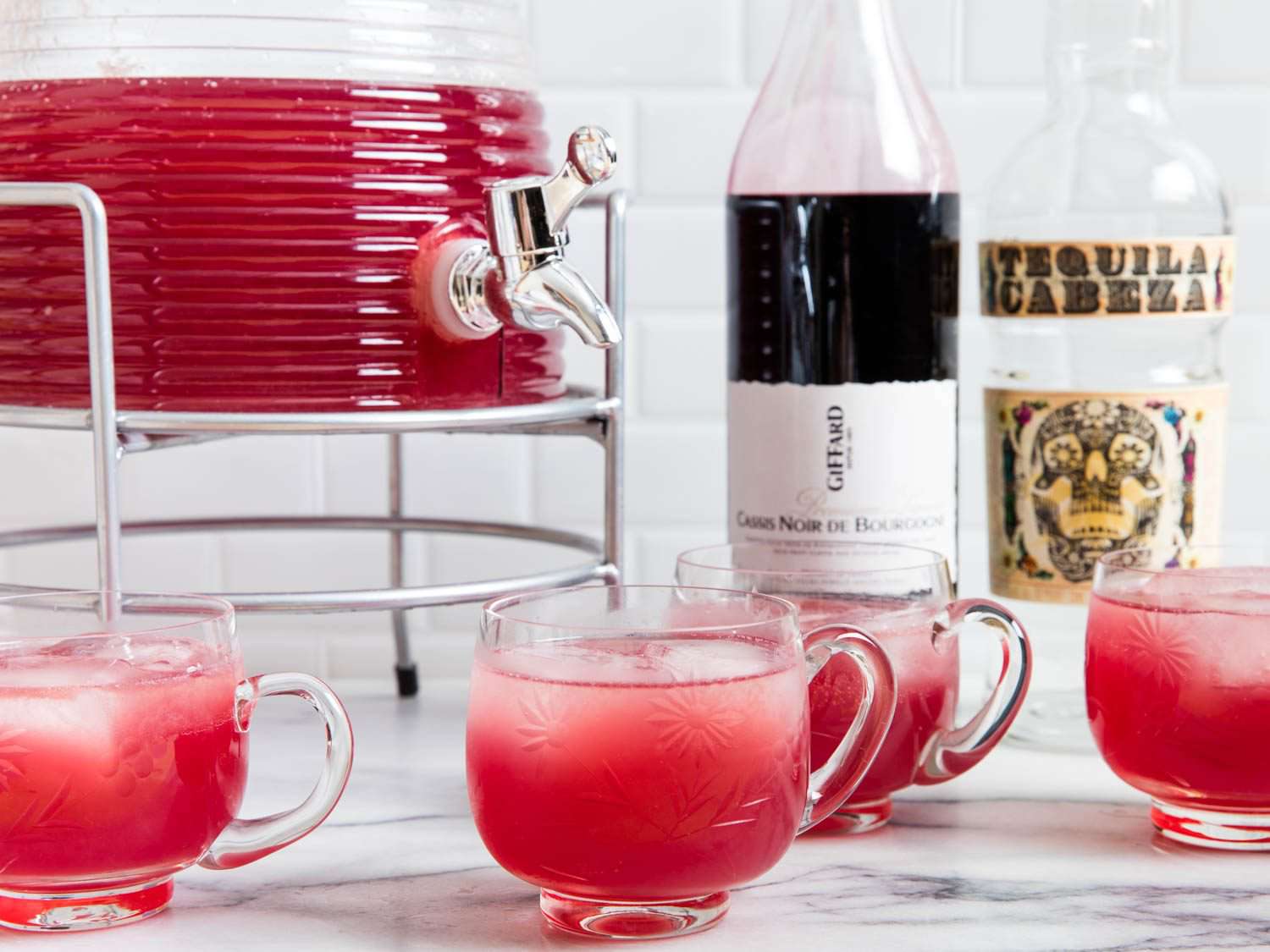 Tequila punch with cassis and lemon in dispenser displayed with filled punch glasses