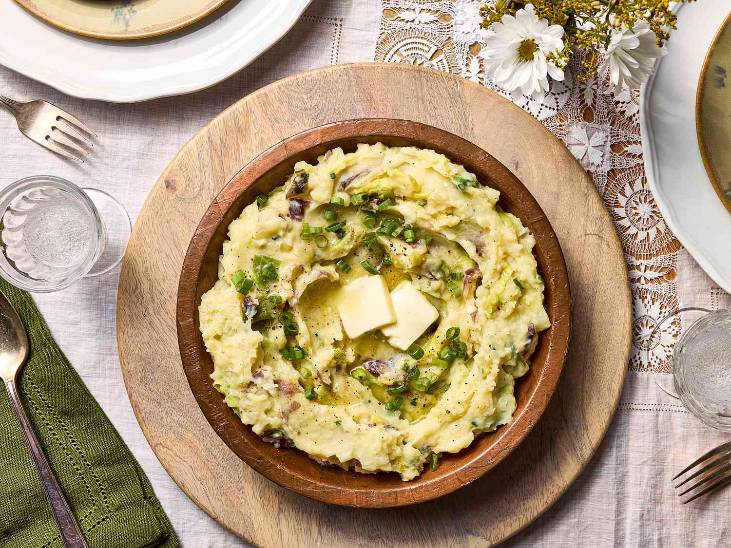 wooden bowl filled with colcannon with butter in it, on a lace tablecloth with flowers to the side