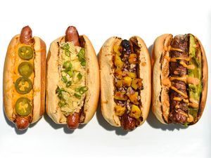 Overhead view of four hot dogs on a white surface, garnished with a variety of topping combinations.