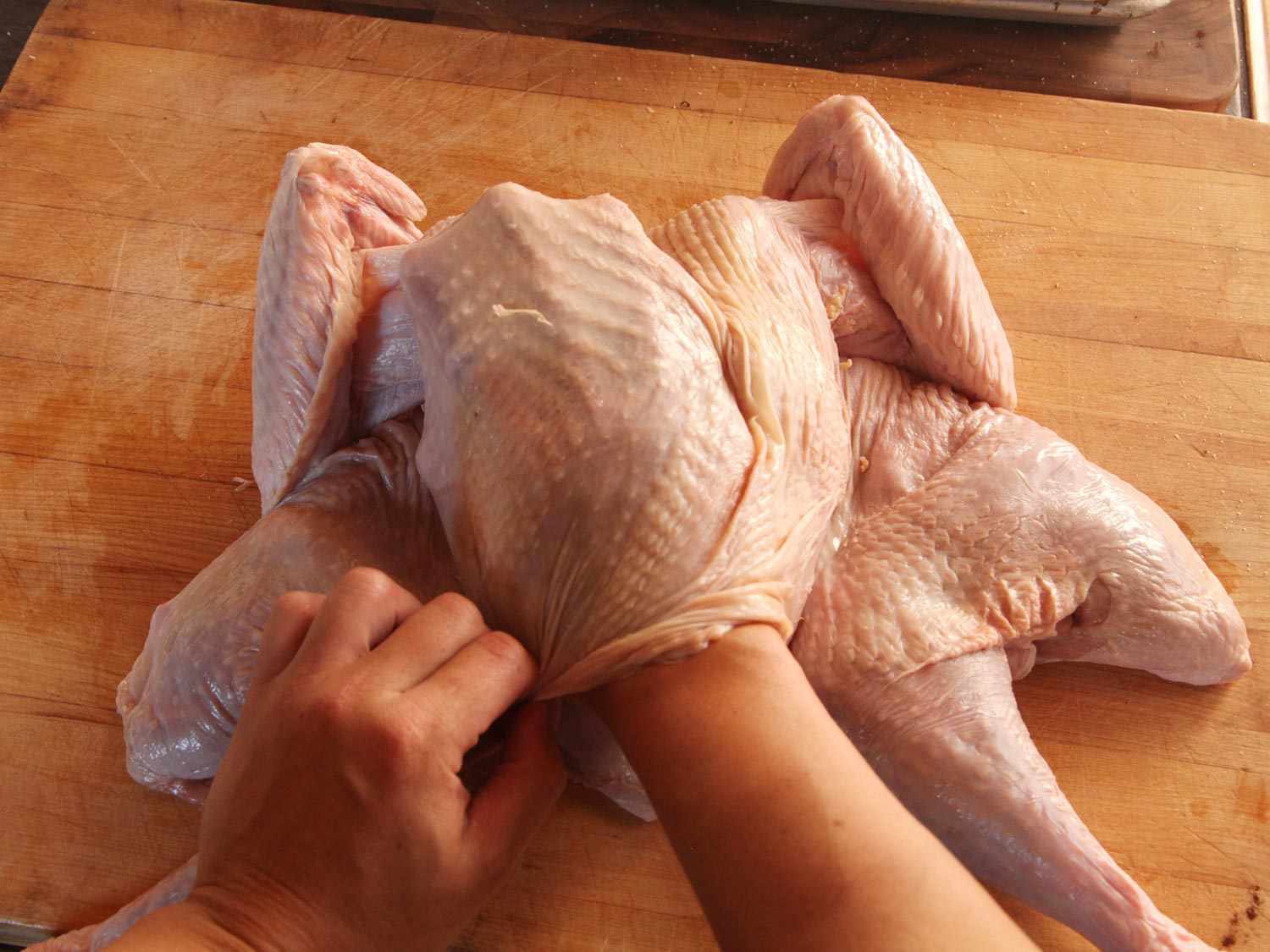 A hand separating uncooked turkey skin from the turkey so butter may be distributed underneath the skin.