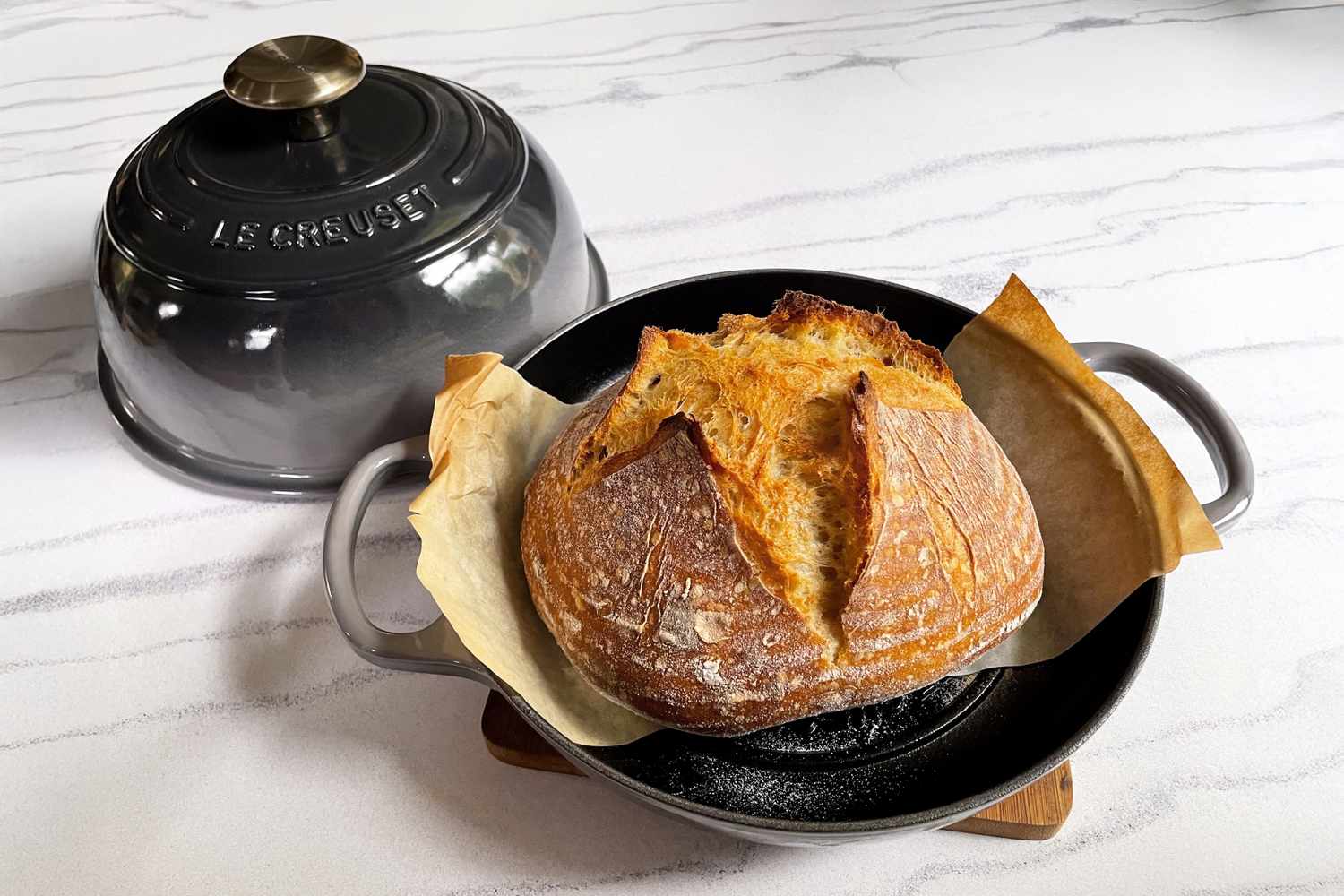 A loaf of bread in a Le Creuset cast iron bread oven set on a countertop
