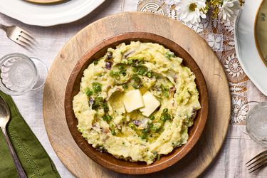 wooden bowl filled with colcannon with butter in it, on a lace tablecloth with flowers to the side