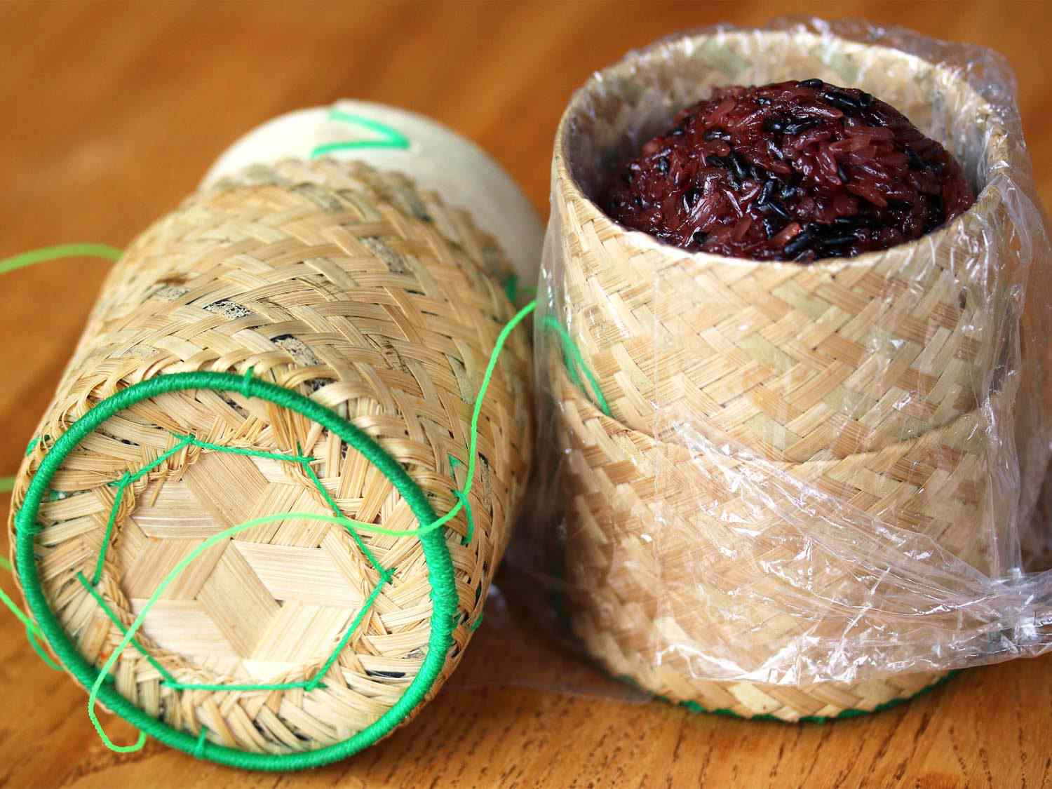 A woven basket (thip khao) with a cover, holding a mound of dark grains of sticky rice (khao niew).