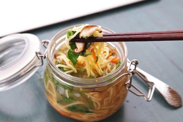 A clip top jar full of homemade instant noodles. A pair of chopsticks lifts a bite from the jar.