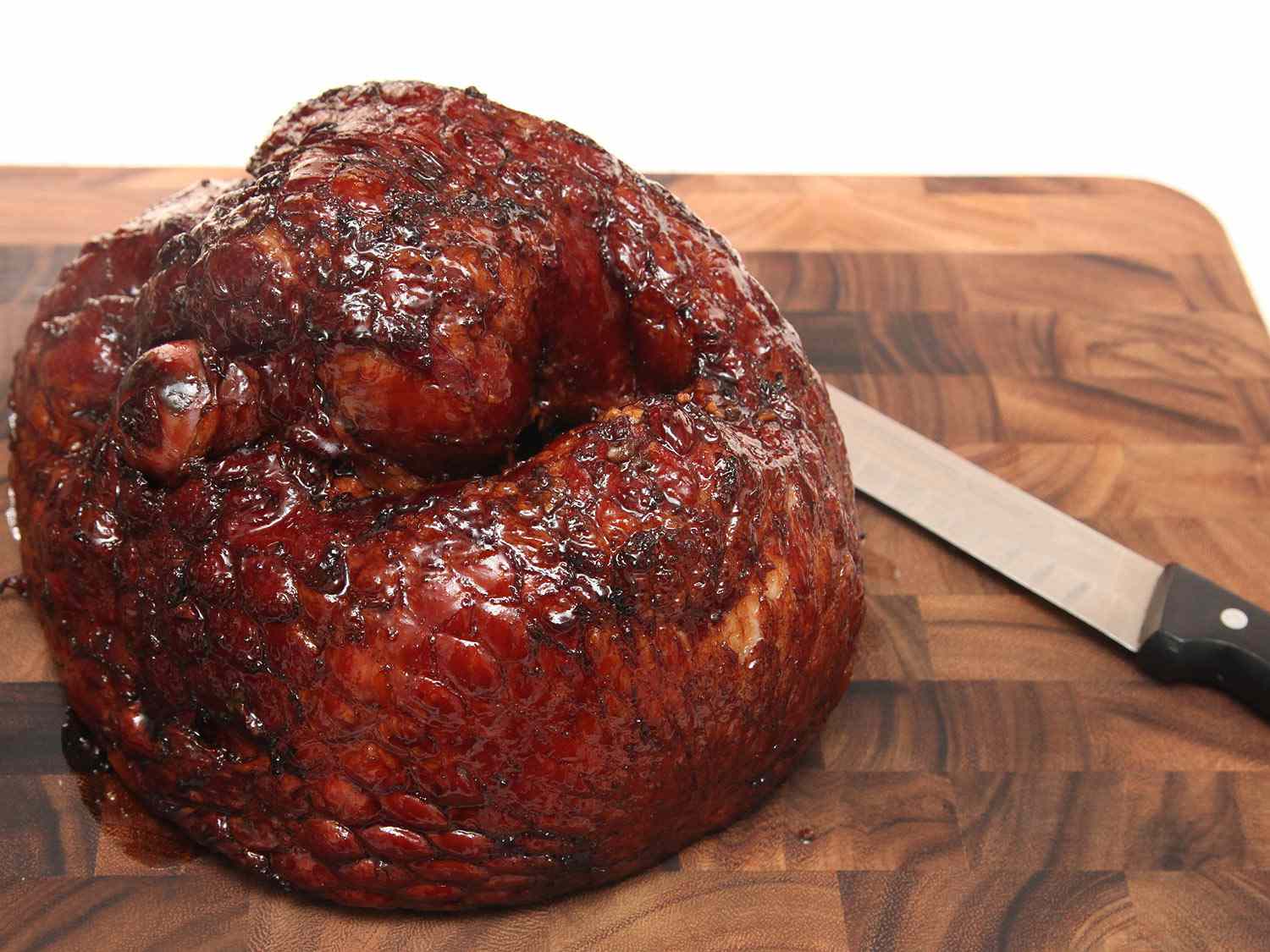A glazed ham on a cutting board ready to be carved.