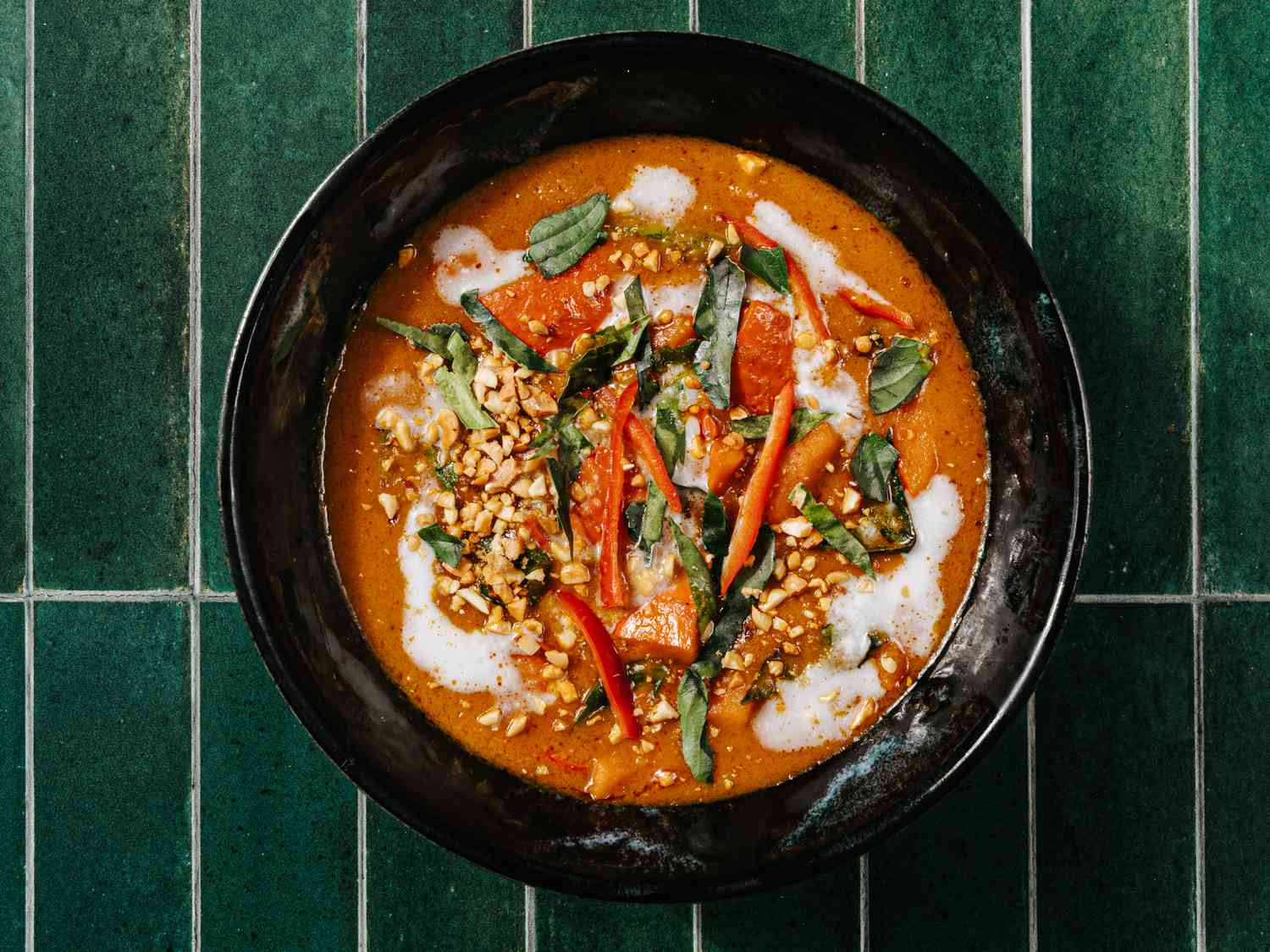 Squash Panang curry in a black bowl, with all the toppings added on a deep green tile surface.