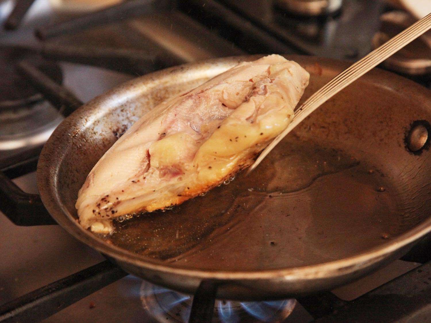 Lifting the bottom of a sous vide cooked chicken breast in a pan as it browns.
