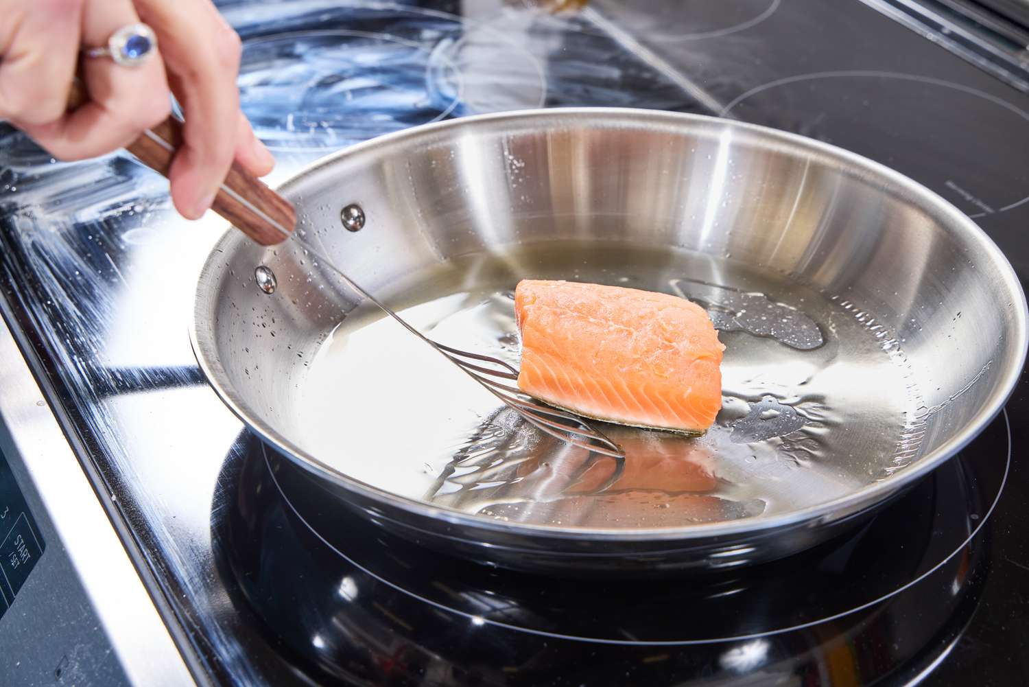 A person cooks salmon in the All-Clad D3 Stainless-Steel 12-Inch Fry Pan