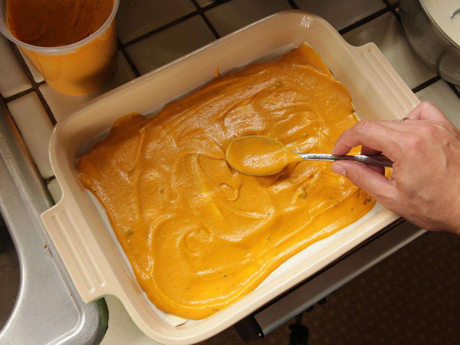 Smoothing squash puree over pasta sheets in a baking dish.