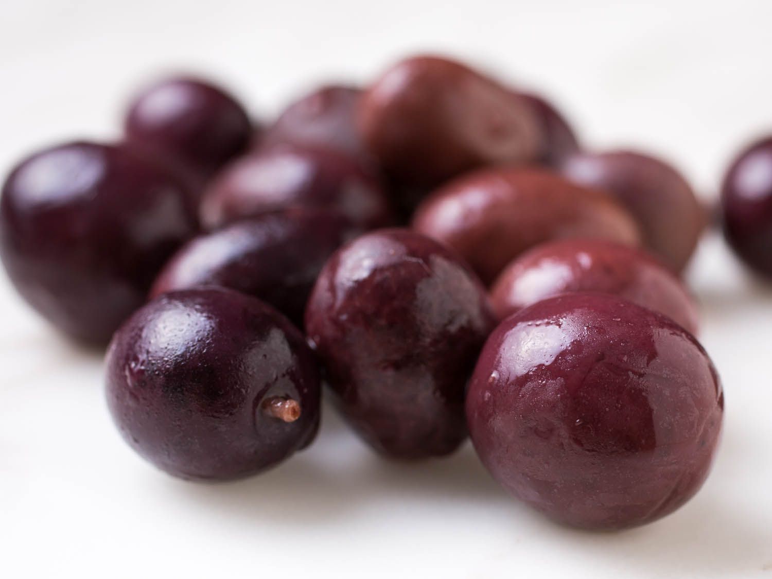 Closeup of maroon-colored olives on white surface