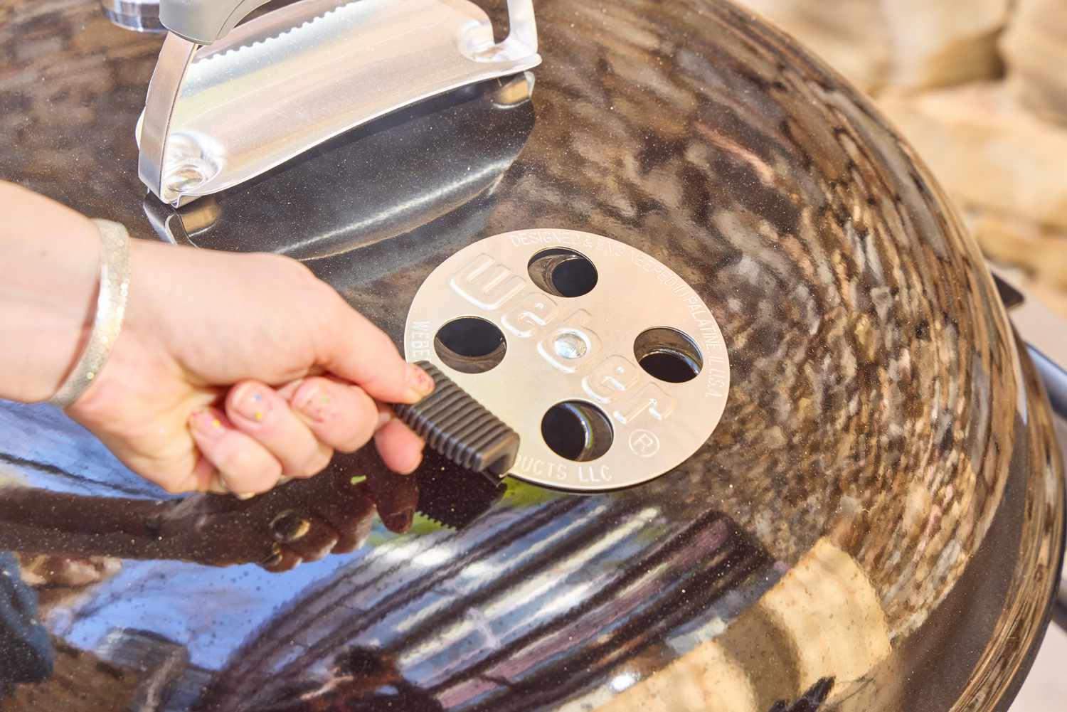 A hand touching the top of the Weber Performer Deluxe Charcoal Grill 22