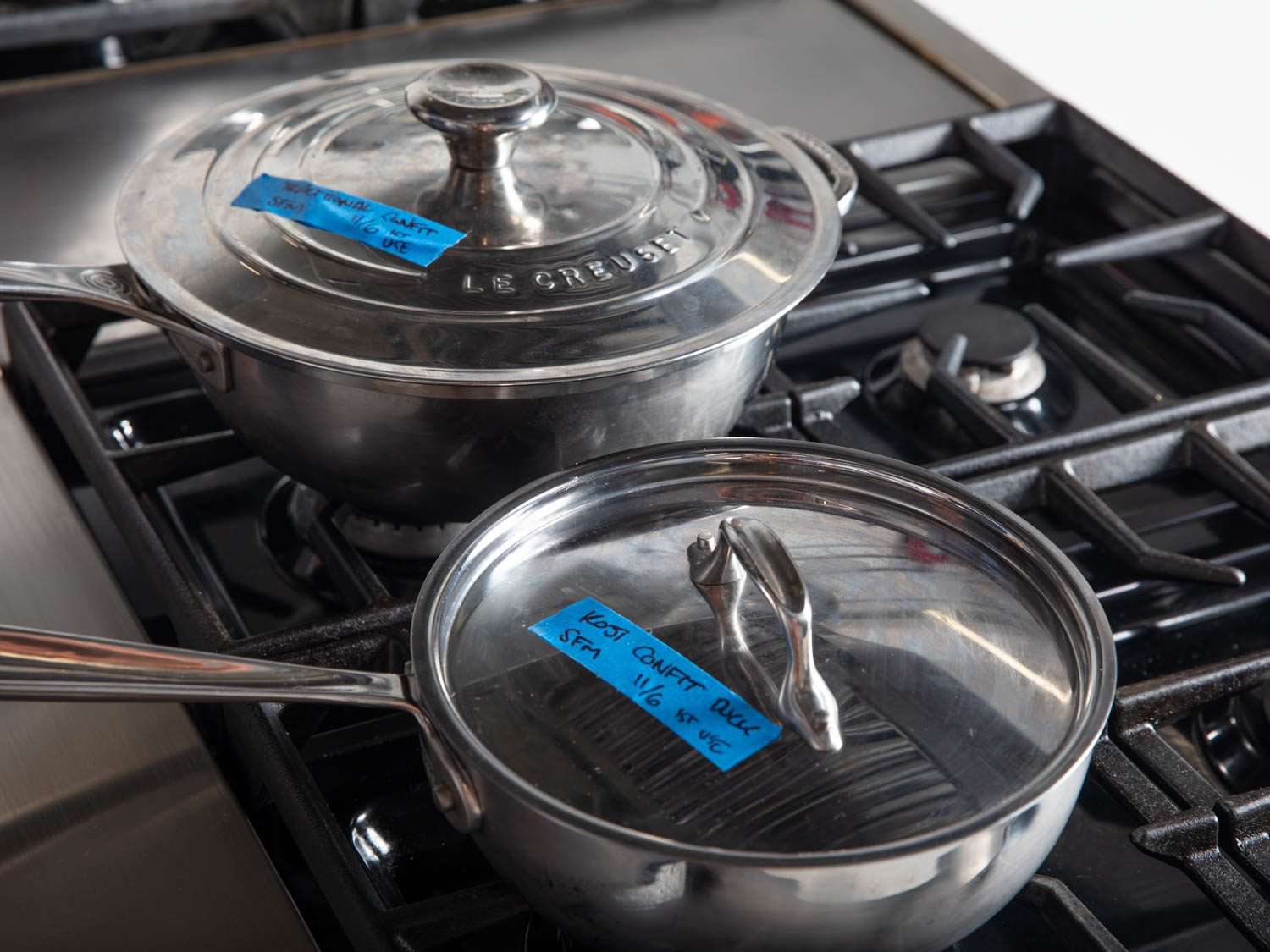 Two lidded saucepans with duck confit on stovetop.