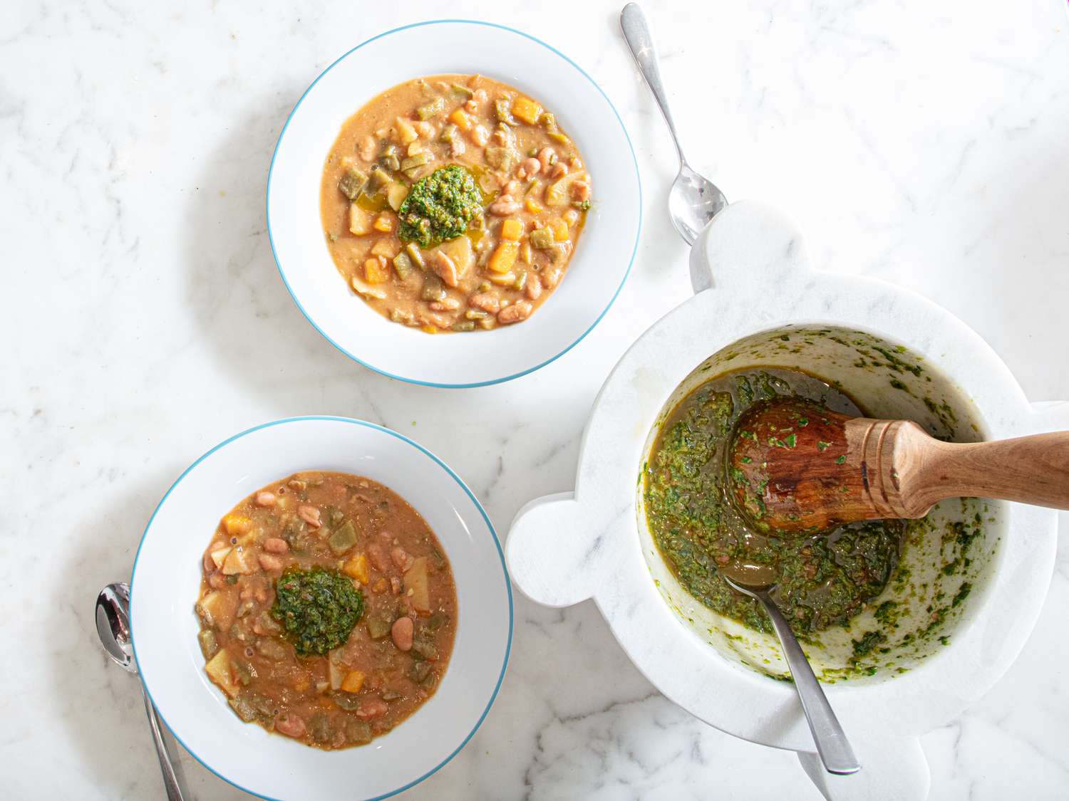 Two bowls of stew garnished with sauce alongside a mortar and pestle with sauce