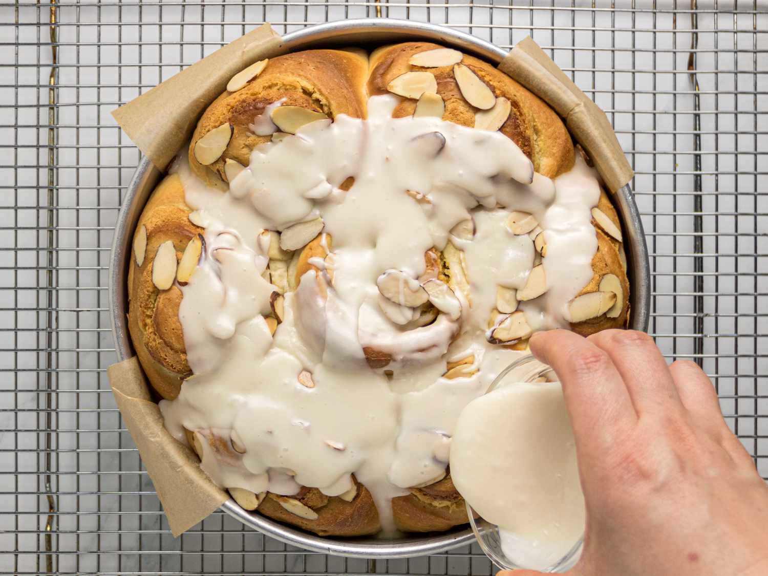 pouring frosting on baked rolls on a cooling rack 