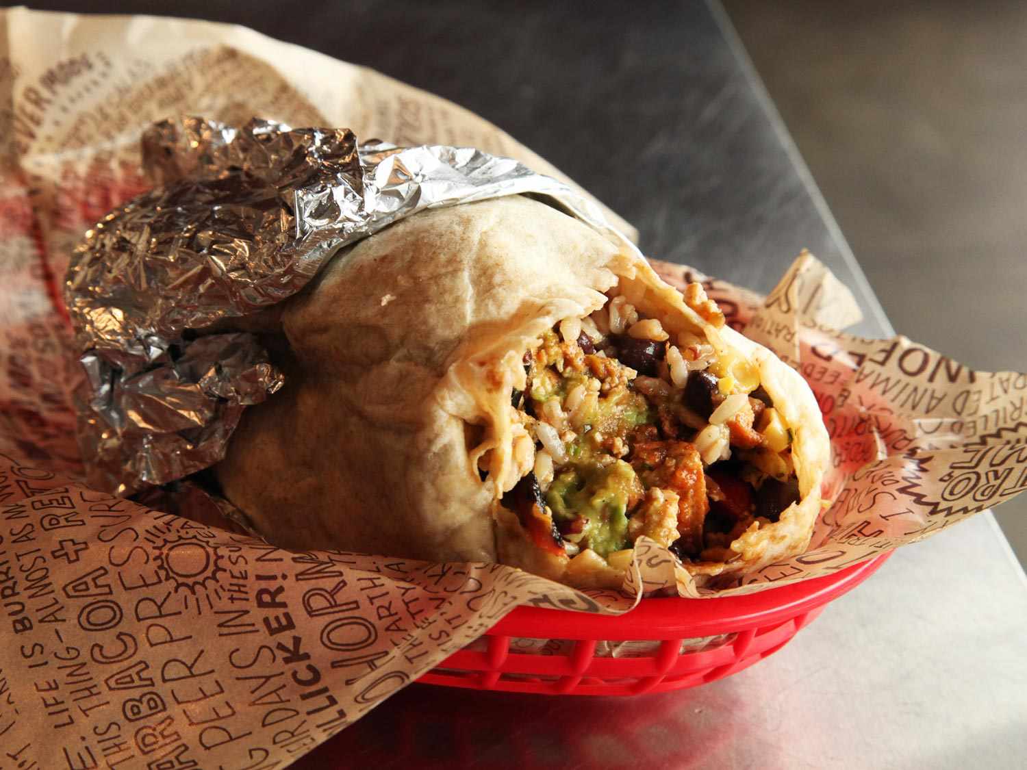 A sofritas burrito with a bite taken out of it in a red plastic tray at Chipotle
